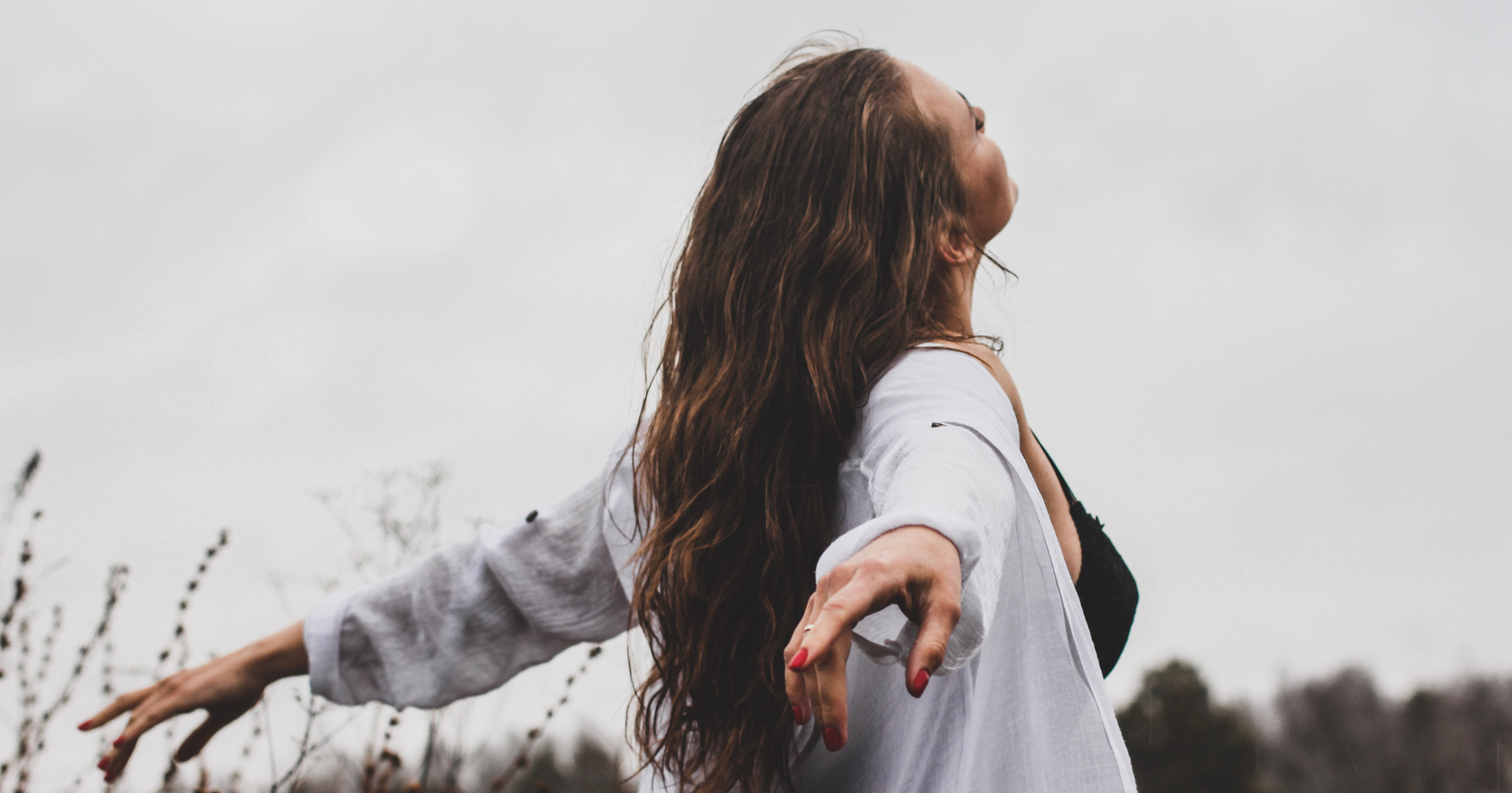 Zdjęcie poglądowe: Kobieta wśród przyrody, z szeroko rozłożonymi do tyłu rękami, wypchniętą klatką piersiową i uniesioną głową, w pozycji sugerującej wyzwolenie. Mechanizm uwalniania emocji w Klasycznej Medycynie Chińskiej - Jak wzmacniać ciało energetycznie?